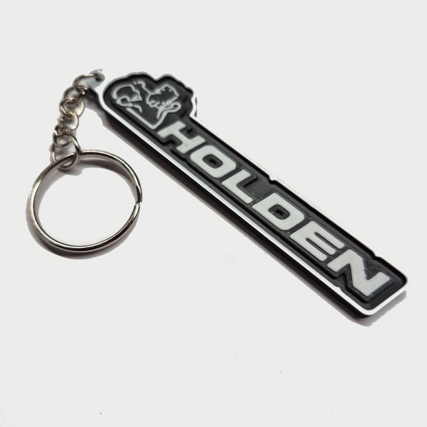 A black and silver Holden keychain featuring the brand's name and logo, attached to a silver split key ring, set against a plain light gray background.