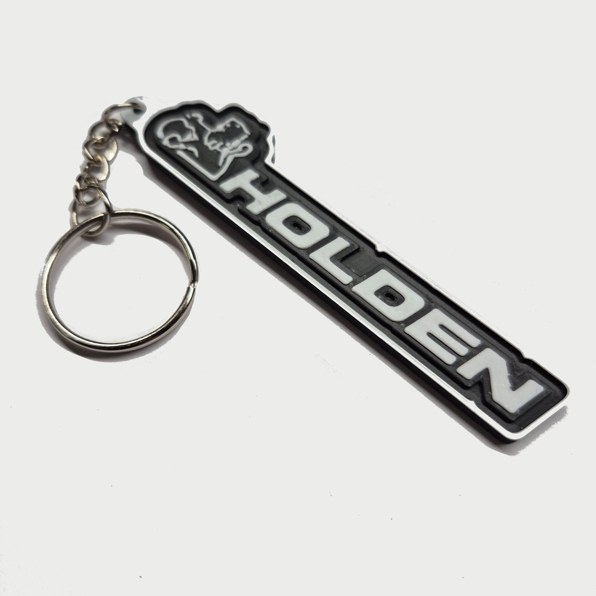 A black and silver Holden keychain featuring the brand's name and logo, attached to a silver split key ring, set against a plain light gray background.