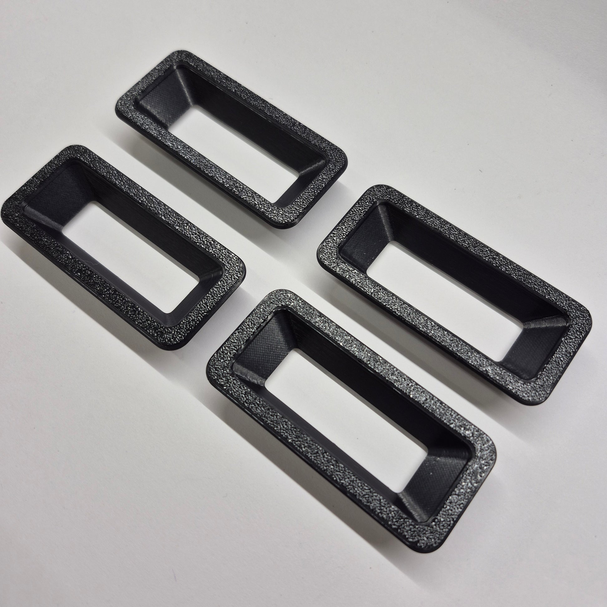 Four black rectangular baking pans with speckled texture on a light gray background