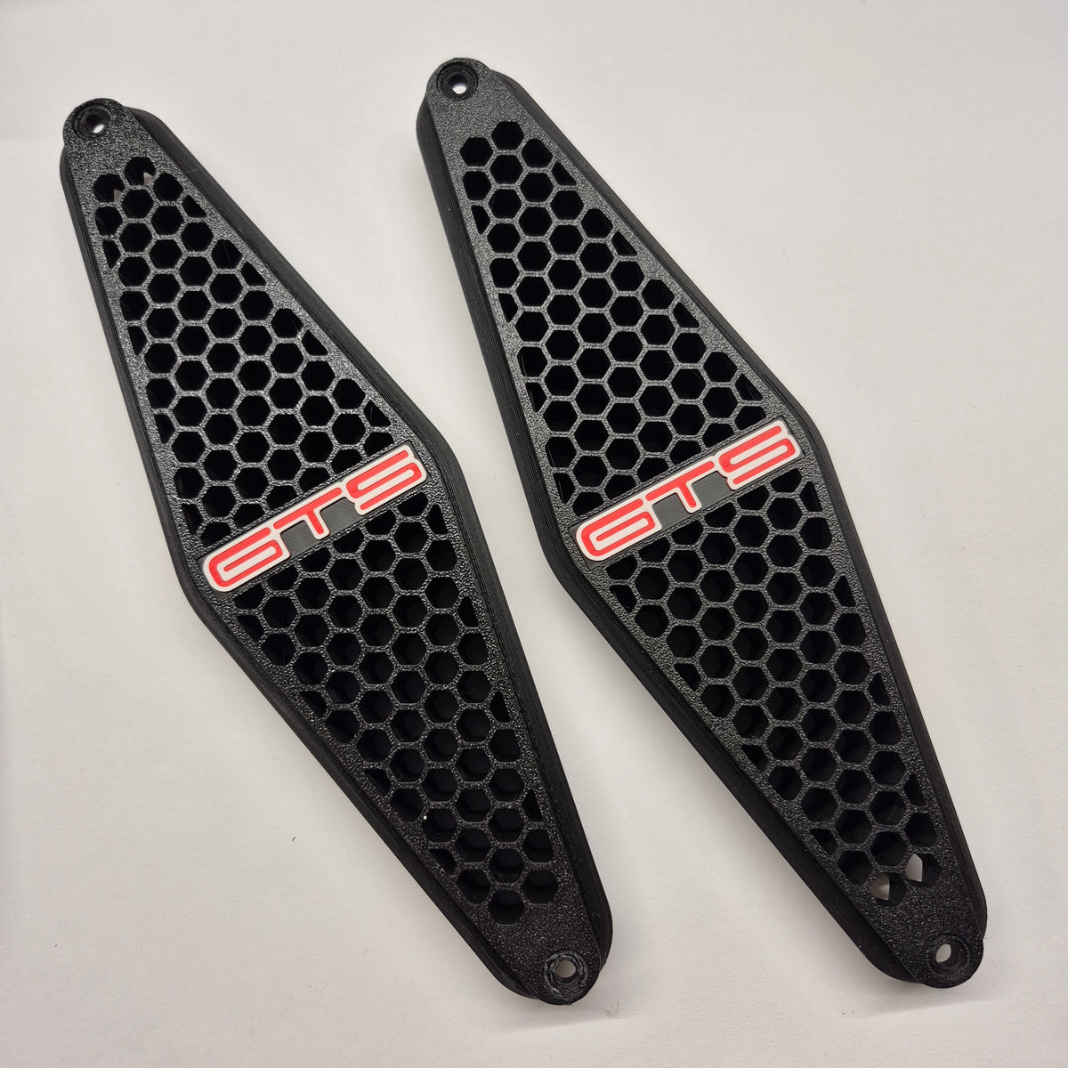 A pair of black honeycomb-patterned protective covers with red 'GTS' lettering, displayed on a light gray background.
