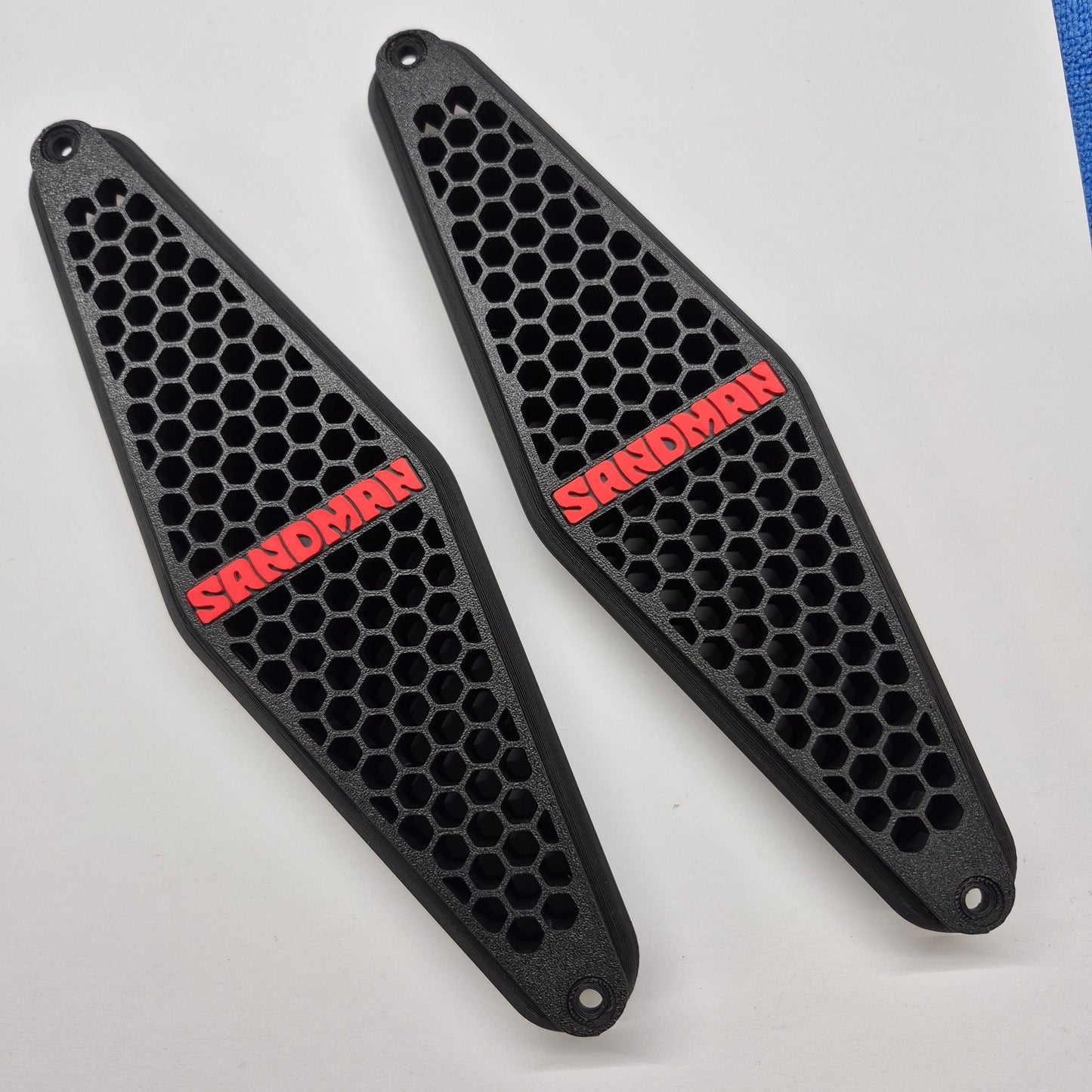 A pair of black motorcycle tank covers with a honeycomb pattern and red 'SANDMAN' branding, displayed on a white background.