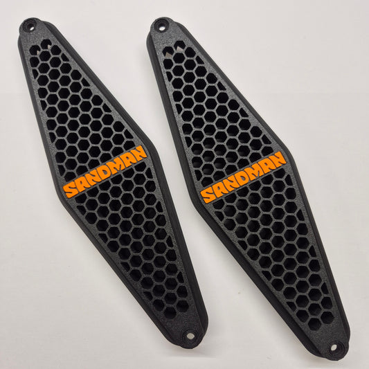 Two black honeycomb-patterned sandboard/skating pads with orange 'SANDMAN' branding, displayed on a light gray background.