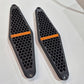 Two black honeycomb-patterned motorcycle foot pegs with orange branding on a white background