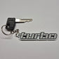 A black and white keychain featuring a stylized 'MUGUE' logo, shown with a metal key and keyring on a light gray background.