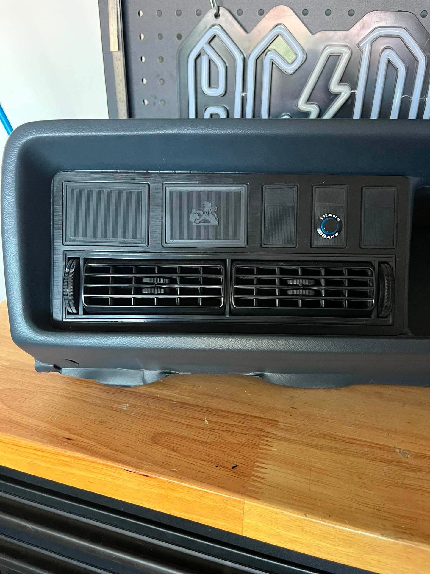 Car air conditioning vent on a wooden surface with a pegboard in the background