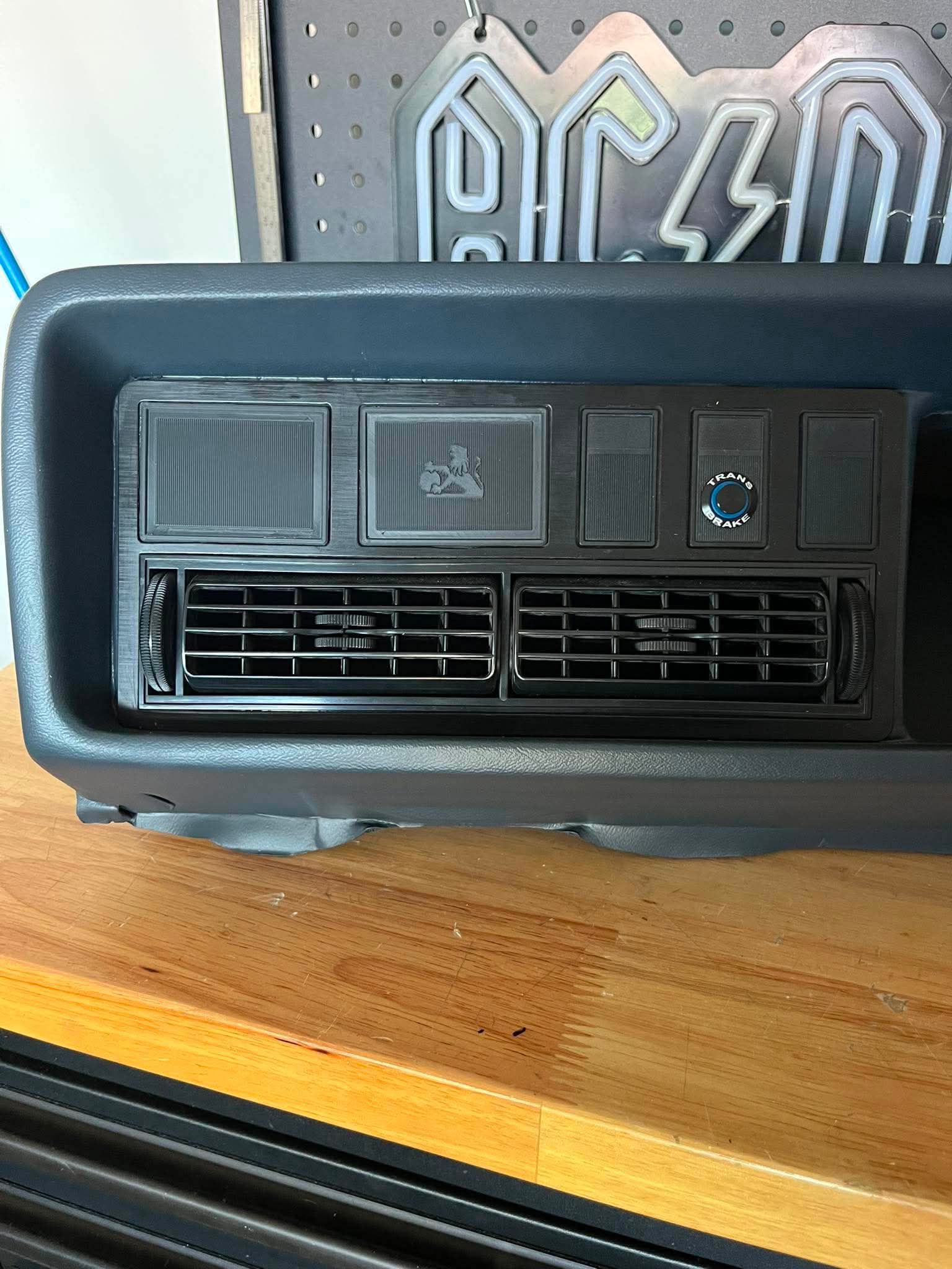 Car air conditioning vent on a wooden surface with a pegboard in the background