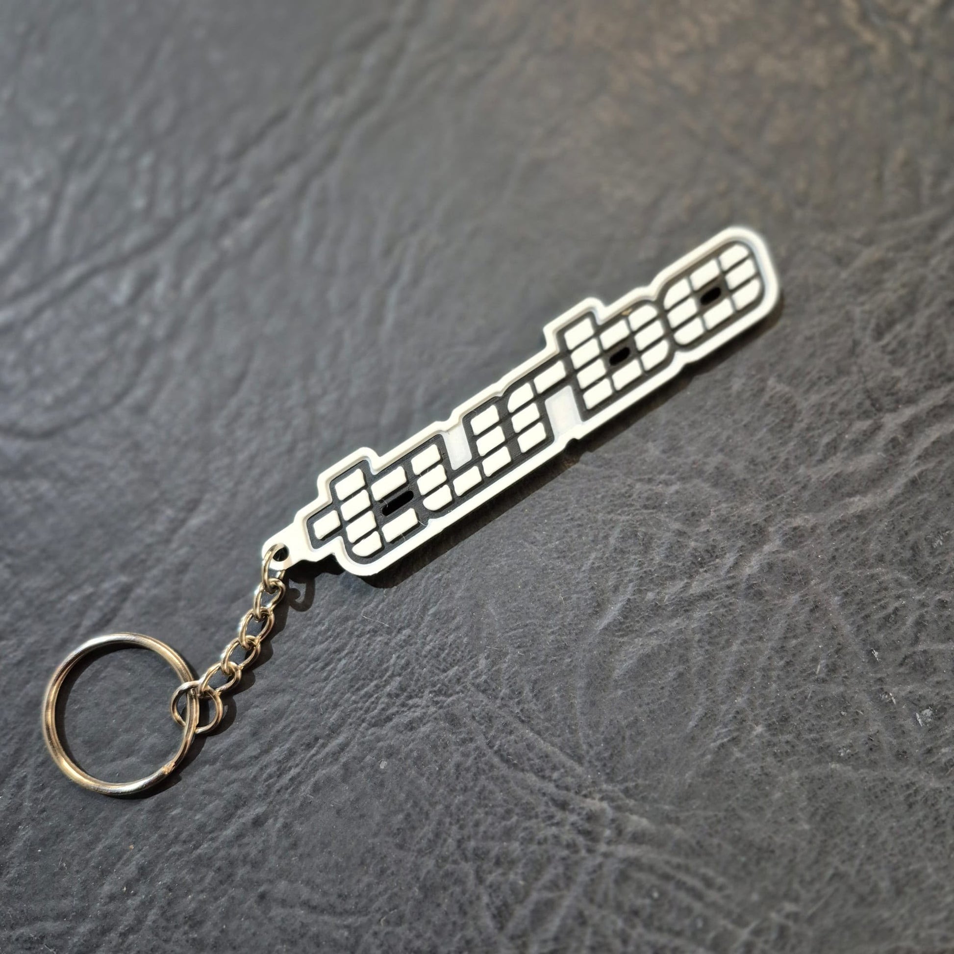 A silver metal keychain featuring a stylized 'turbo' wordmark with a checkered flag motif, attached to a split key ring and resting on a dark textured surface.