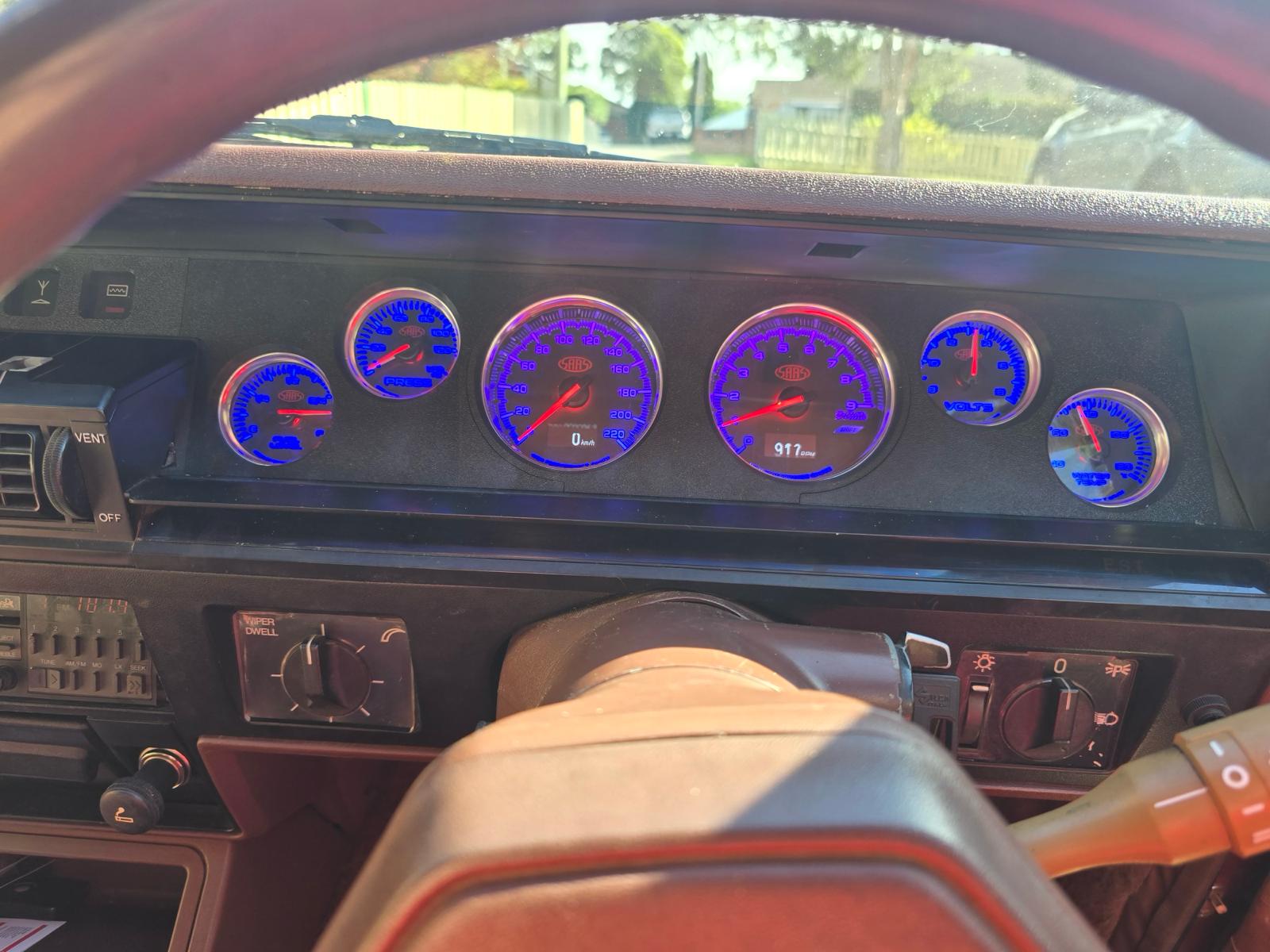 Car dashboard with illuminated gauges and a person's leg in the foreground